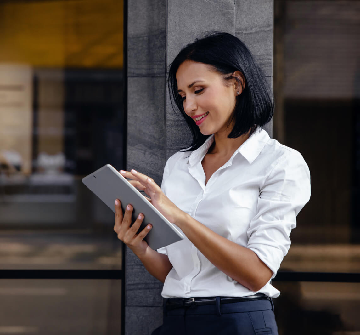 Lady Leaning Against A Wall Smiling While Using An Ipad
